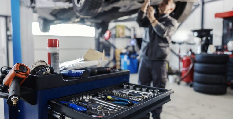 Cropped picture of a mechanic toolbox with tools in drawer with worker repairing car in blurry background at workshop.